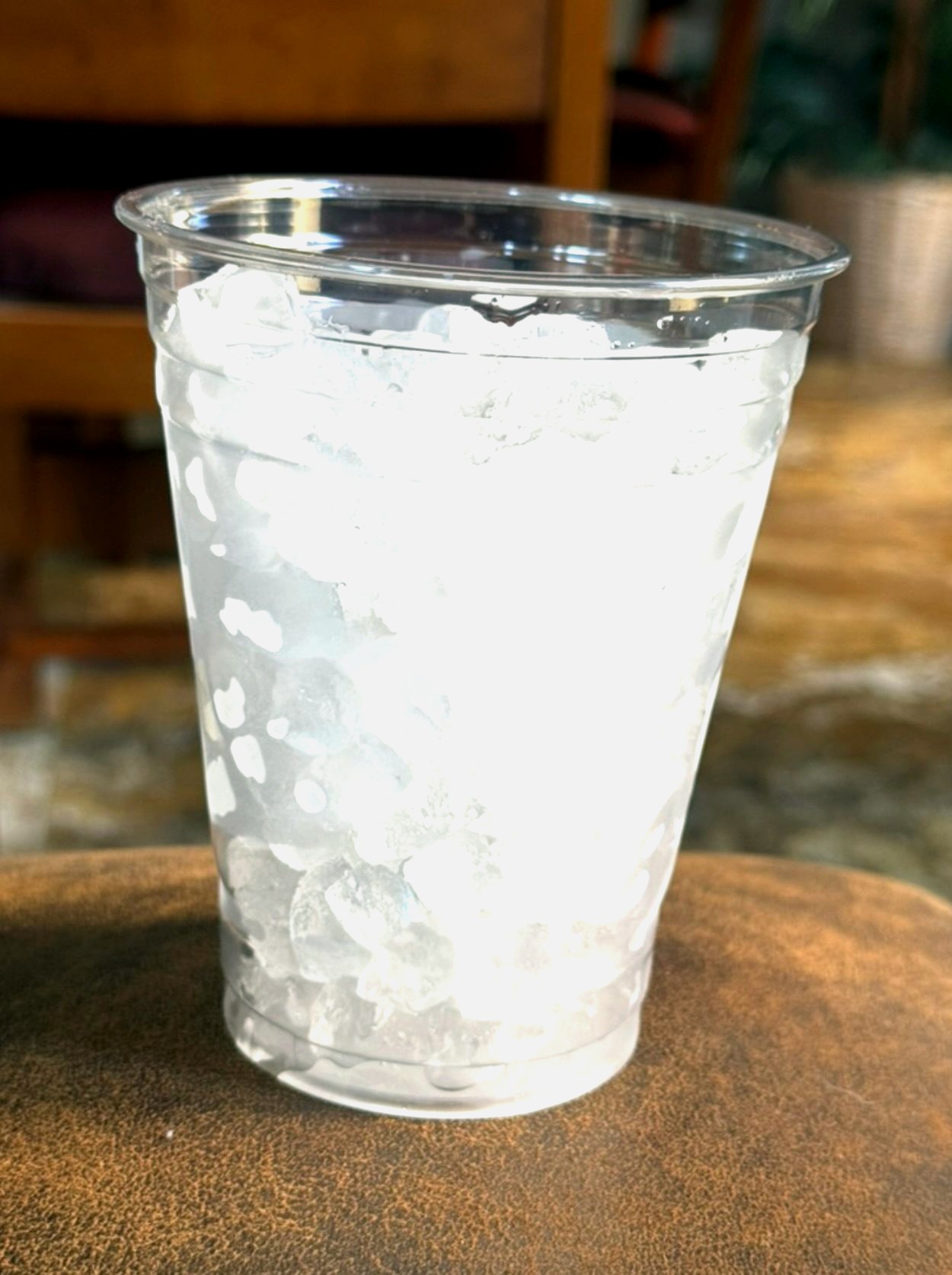 A tall clear cup of nugget ice, photographed on a leather ottoman, awaiting a beverage worthy of it.