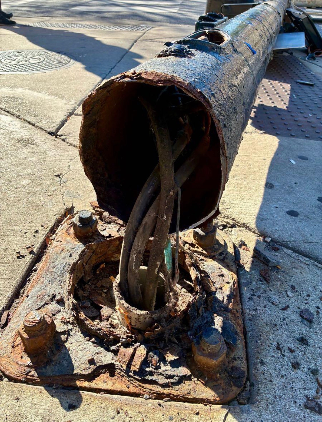 Rusted, broken pole above its mounting plate, with exposed cables